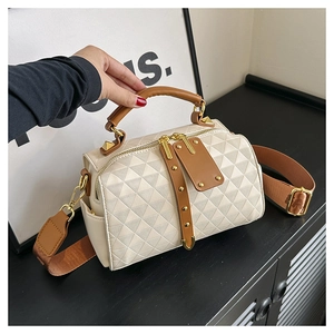 Detail of cream quilted handbag featuring brown leather trim and adjustable wide strap