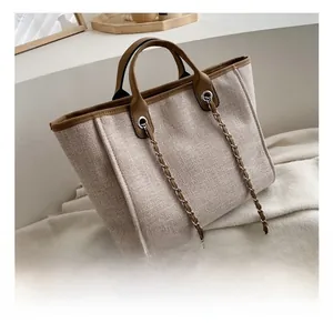 Detail of canvas tote bag showing brown leather trim and metal chain shoulder strap