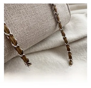 Detail of silver metal chain strap woven with brown leather on a beige tote bag