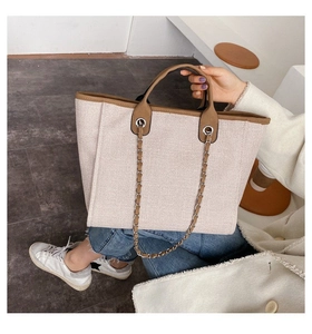 Detail of woven canvas tote bag featuring brown leather trim and metallic chain strap