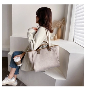 Detail of canvas tote bag with brown leather trim and metal chain shoulder strap
