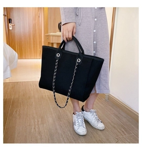 Detail of a large black canvas tote bag featuring a chain shoulder strap and woven edges