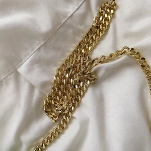 Close-up of a thick golden cuban link chain strap on a white wrinkled fabric surface