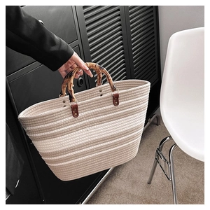 Detail of woven tote bag with natural bamboo handles and textured striped knit fabric
