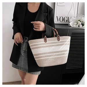 Close-up of woven striped tote bag with bamboo handles held by a model in casual wear