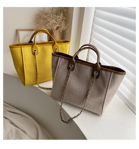 Detailed view of canvas tote bag featuring premium leather trim and chain decoration