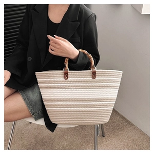 Detail of woven tote bag with natural bamboo handles and striped gradient pattern design