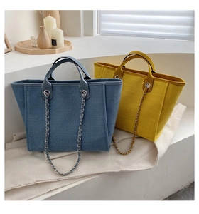 Detailed close-up of textured canvas tote bags in denim blue and bright yellow with chain strap