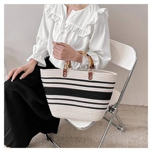 Detail of woven tote bag featuring natural bamboo handles and striped fabric texture