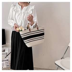 Close-up of woven tote bag featuring black and white stripes and natural bamboo handles