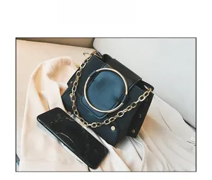Detail view of small black leather crossbody bag with gold ring and smartphone for scale