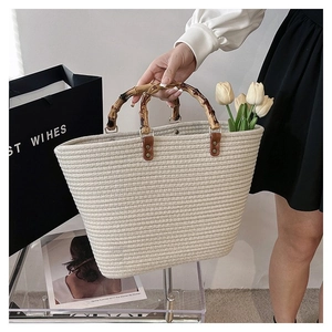 Detail of woven straw tote bag featuring bamboo handles and premium leather accents