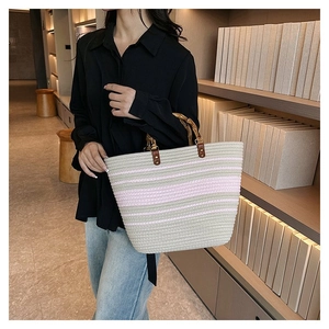 Detail of striped woven tote bag featuring natural bamboo handles and leather fasteners