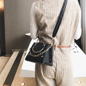Close-up of black leather crossbody bag with gold ring handle and chain on model