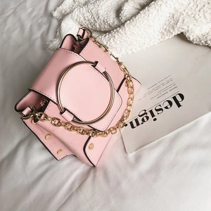Detail view of pink crossbody bag with golden ring handle and metal chain on white cloth