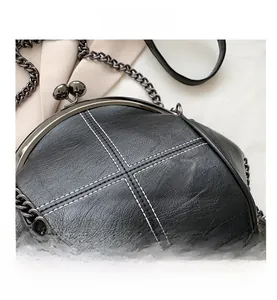Detail of black leather shell bag featuring white cross-stitch and metal clasp
