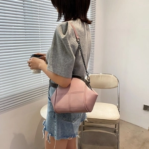 Detail of pink shell crossbody bag with cross stitching and chain strap on a model