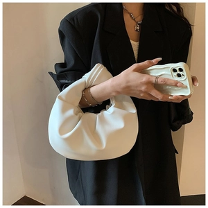 Detail of white pleated cloud handbag showing soft leather texture held by a model