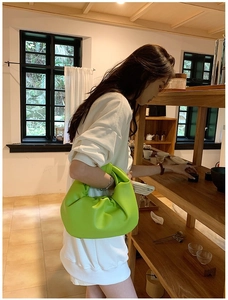 Detail of lime green ruched dumpling bag with signature knot handle on casual outfit