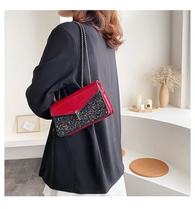 Détail du sac à chaîne pailleté rouge et noir porté avec un blazer noir élégant