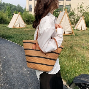 Outdoor shot of a straw tote bag with black stripes and brown leather shoulder straps