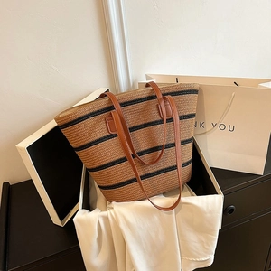 Macro detail of hand-woven straw tote with black stripes and brown leather handles