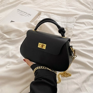 Minimalist black leather crossbody bag with gold twist handle and chunky chain strap