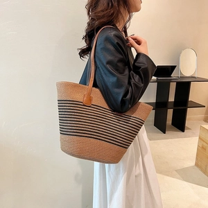Detail of woven straw tote bag with black stripes and brown leather handles on shoulder