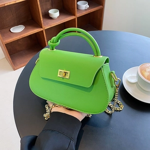 Bright green leather crossbody bag with knot handle and gold chain on a black table