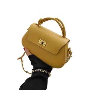 Minimalist ginger leather shoulder bag with gold chain and top knot handle on white backdrop