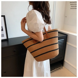 Woven tote bag with black stripes and brown leather straps worn by a model in white