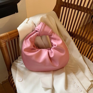 Pink pleated knot handle handbag in vegan leather on a wooden chair with warm lighting
