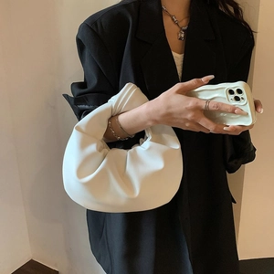 White ruched cloud handbag with knot handle detail held by model in black suit