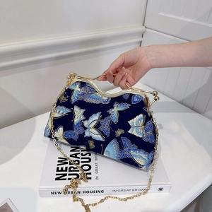 Close-up of blue satin evening bag with butterfly embroidery and wavy metal handle