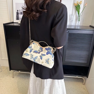 Detail of vintage cream handbag with blue butterfly print and elegant metal clasp handle