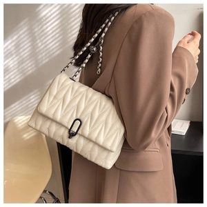 Sac bandoulière matelassé beige avec chaîne en métal porté par un mannequin sous la lumière