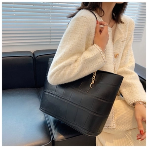 Detail view of black crocodile pattern tote bag with metal chain strap on model