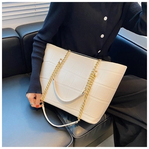 Detail showing white crocodile-textured tote bag with gold chain strap on model