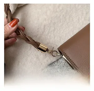 Détail du fermoir mousqueton doré et de la bandoulière en cuir marron tressé du sac