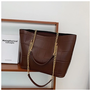 Detail of dark brown tote bag with crocodile texture and gold chain link handle