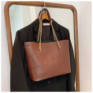 Detail of dark brown crocodile embossed leather tote bag with gold chain strap detail