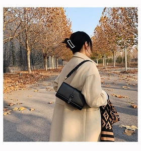 Sac sous le bras chic en cuir litchi noir avec bandoulière tressée porté par un modèle