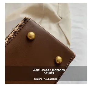 Detail of brown faux leather bag bottom with houndstooth trim and gold protection studs