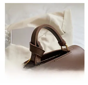 Close-up of thick dark brown leather handle and brushed gold hardware on hand bag