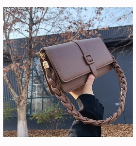 Détail d'un sac à main en cuir beige avec une grosse anse tressée et des boucles dorées