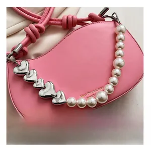 Detail view of pink leather bag featuring large pearl and silver heart chain strap accent
