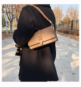 Sac bandoulière en cuir marron avec bandoulière tressée épaisse porté sur manteau noir