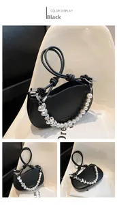 Detail of black crescent shoulder bag featuring pearl and silver heart chain with knot handle