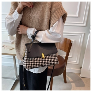 Close-up of black and white houndstooth handbag with leather flap and gold lock detail