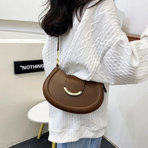 Detail of a brown leather crescent shoulder bag with elegant gold metal buckle on a model